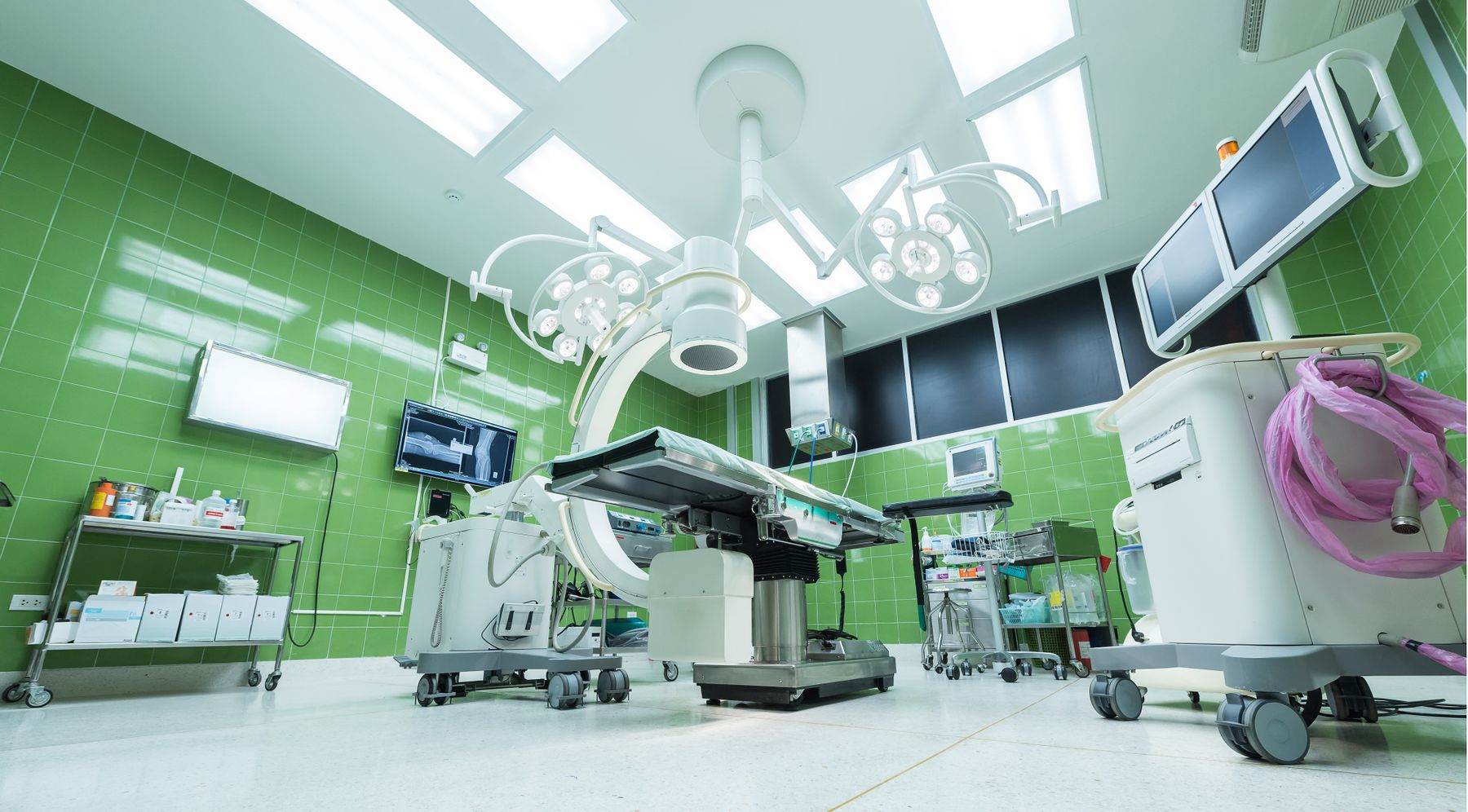 A modern, well-lit clinical theatre with organised equipment and calm green surfaces.